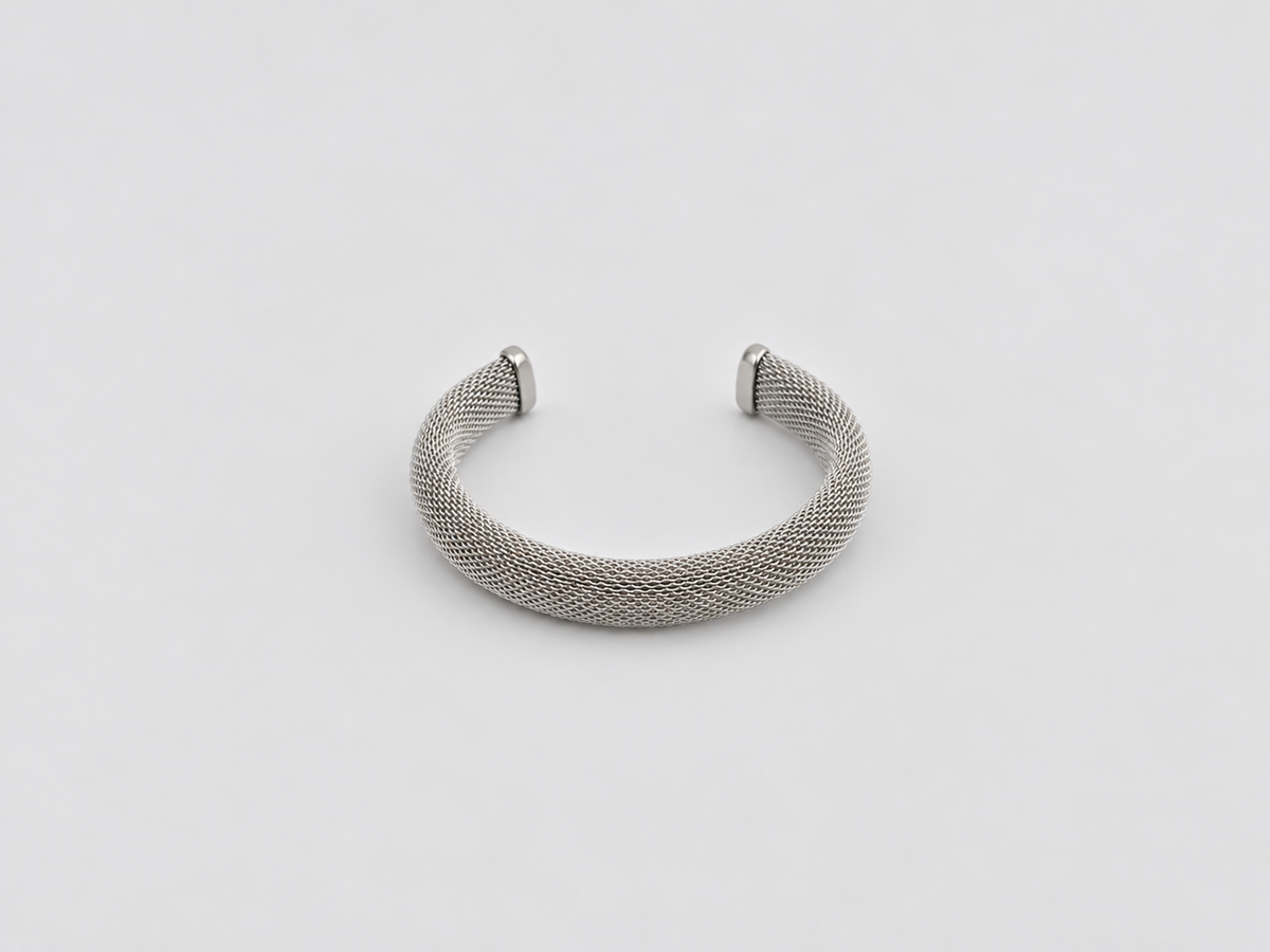 Pulsera Laura, brazalete abierto plateado de malla metálica entrelazada con extremos lisos, sobre fondo gris claro.