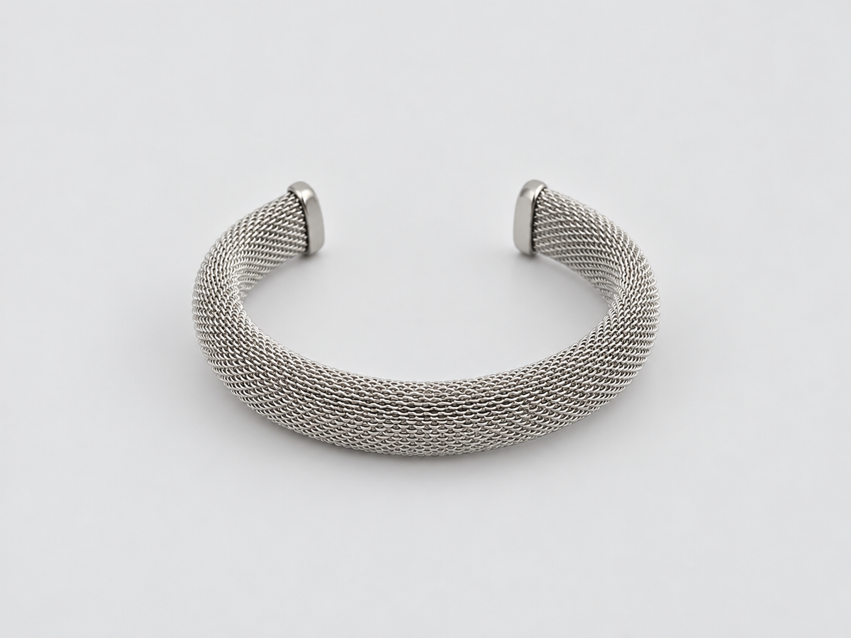 Pulsera Laura, brazalete abierto plateado de malla metálica entrelazada con extremos lisos, sobre fondo gris claro.