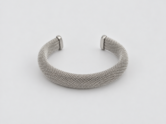 Pulsera Laura, brazalete abierto plateado de malla metálica entrelazada con extremos lisos, sobre fondo gris claro.